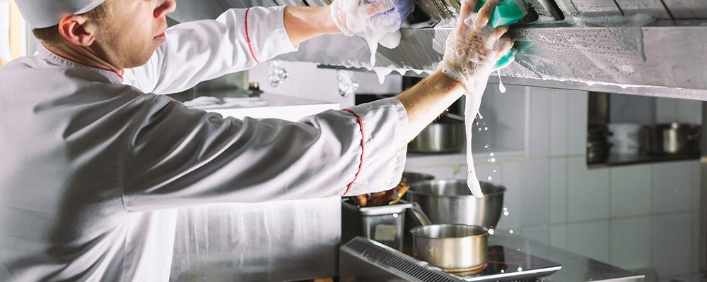 Agent de nettoyage lavant et dégraissant une hotte de cuisine de restaurant avec produits inox